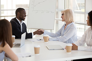 Friendly young african american businessman and smiling mature caucasian businesswoman shaking hands over office table, diverse multiracial partners handshaking at business meeting, respect concept